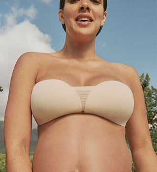 Pregnant woman wearing beige strapless bra that softly curves with her belly